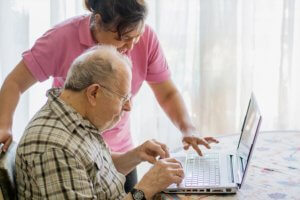 Anciano con cuidadora extranjera felices utilizando el ordenador.