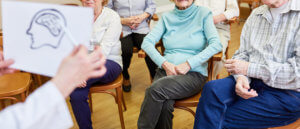 Cuidador mostrando un dibujo de la cabeza de una persona a grupo de ancianos de una asociación de Alzheimer.