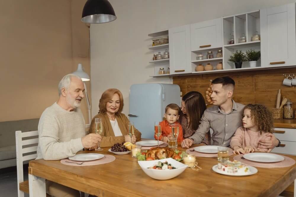 Una familia con los abuelos, hijo, mujer y nietos en una mesa comiendo y brindando. 