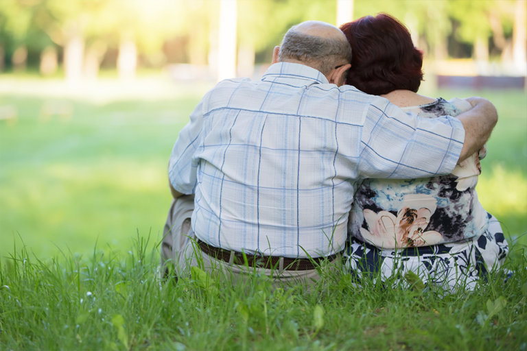 Pareja de ancianos de espaldas sentados en la hierba de un parque.