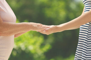 Foto de cuidadora y anciana en verano dándose las manos.