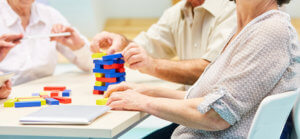 Grupo de ancianos con Alzheimer jugando con unas maderitas de colores que forman una torre.