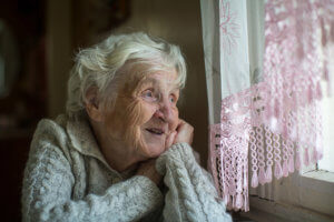 Foto de una anciana de perfil pensativa en su casa.