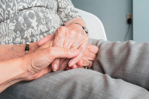Primer plano de manos de cuidadora cogiendo las de anciana tras hospitalizacón.