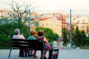 Foto de tres ancianas de espaldas sentadas en un banco de la calle.