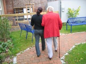 Trabajadora del Hogar con anciana dando de paseo por el jardín.