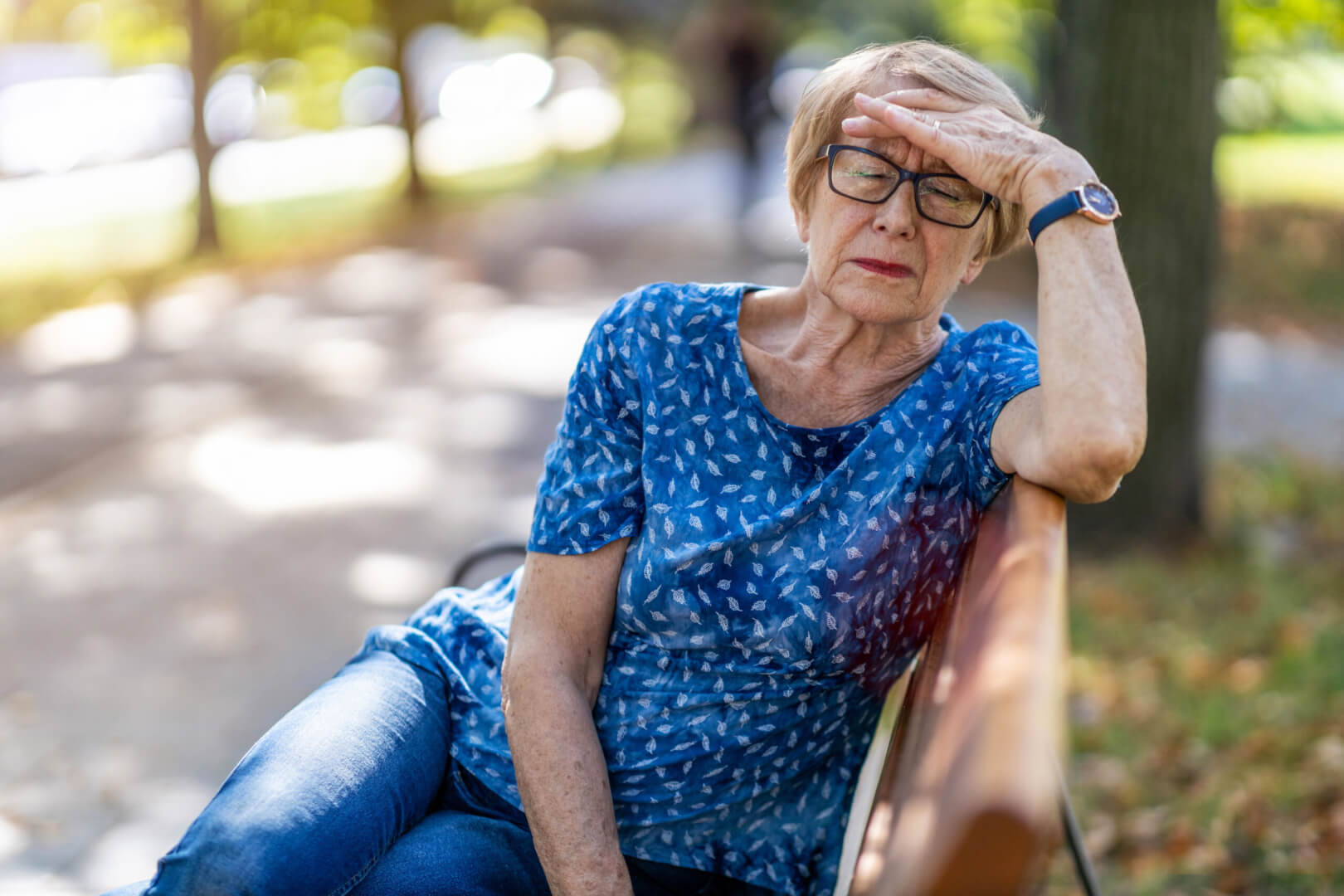 Una señora mayor se encuentra sufriendo un golpe de calor en un banco a la sombra de un parque. 