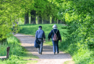 Una abuelo y una abuela paseando por un parque lleno de verde.