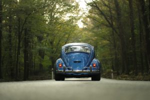 Coche clásico circulando por una carretera por el bosque.