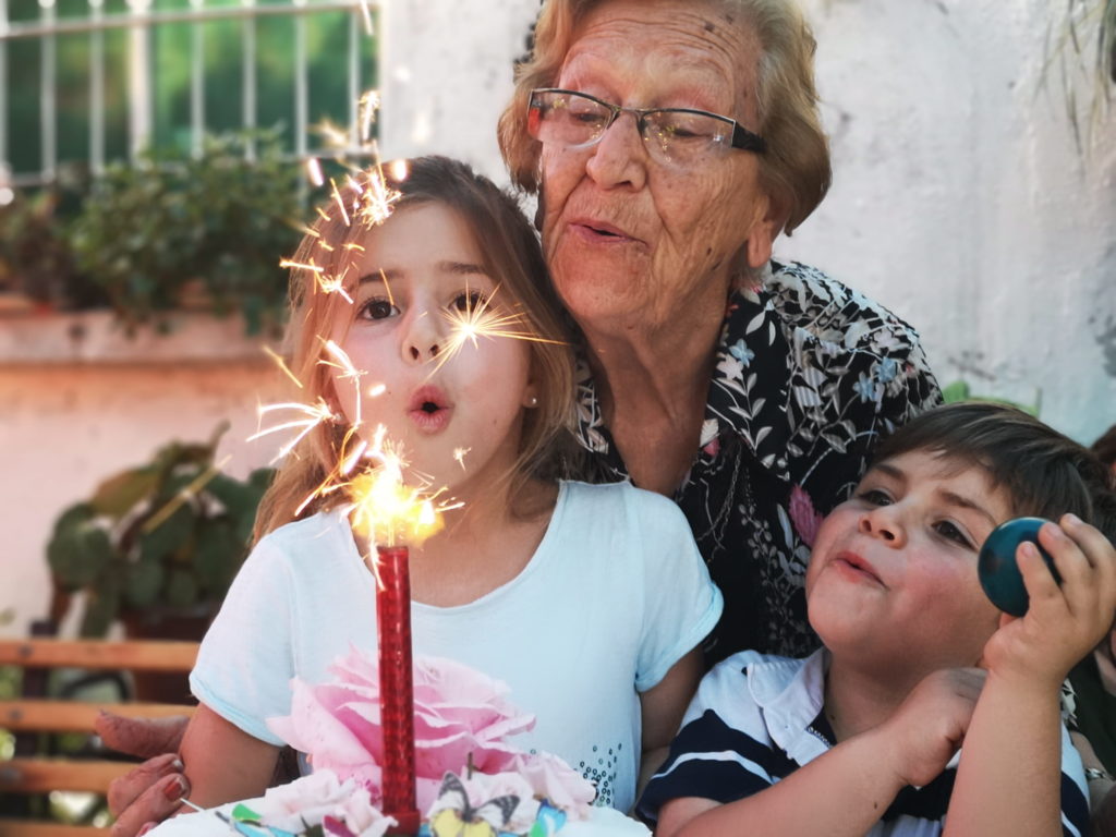 abuelas soplando una tarte de cumpleaños junto a los nietos. 