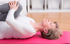 Mujer mayor tumbada en una esterilla de color rosa haciendo estiramientos de pierna debido a problemas de tendinitis.