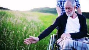 Cuidador paseando con anciano con Alzheimer y silla de ruedas por el campo.