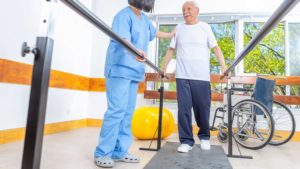 Cuidadora ayudando a anciano con ataxia a hacer rehabilitación.