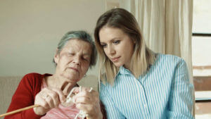 Anciana haciendo ganchillo mientras se lo muestra a su cuidadora.