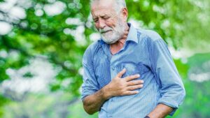 Anciano en el parque con la mano sobre su pecho y dolor pectoral.
