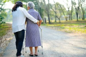 Anciana ayudada por su cuidadora dan un paseo por el parque.