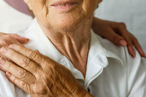 Mujer con las manos sobre los hombros de una anciana sonriente.