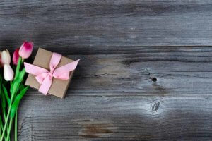 Capullos de rosa blancos y rosados junto a un regalo en una mesa de madera.