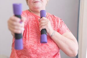 Anciana realizando deporte en casa con una pesa en cada mano.