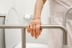 Anciana con estreñimiento sujetándose de la barra junto al retrete.