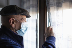Perfil de un anciano con mascarilla mirando por la ventana.