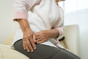 Anciana en la cama tocándose la parte de derecha de la cadera por dolor.