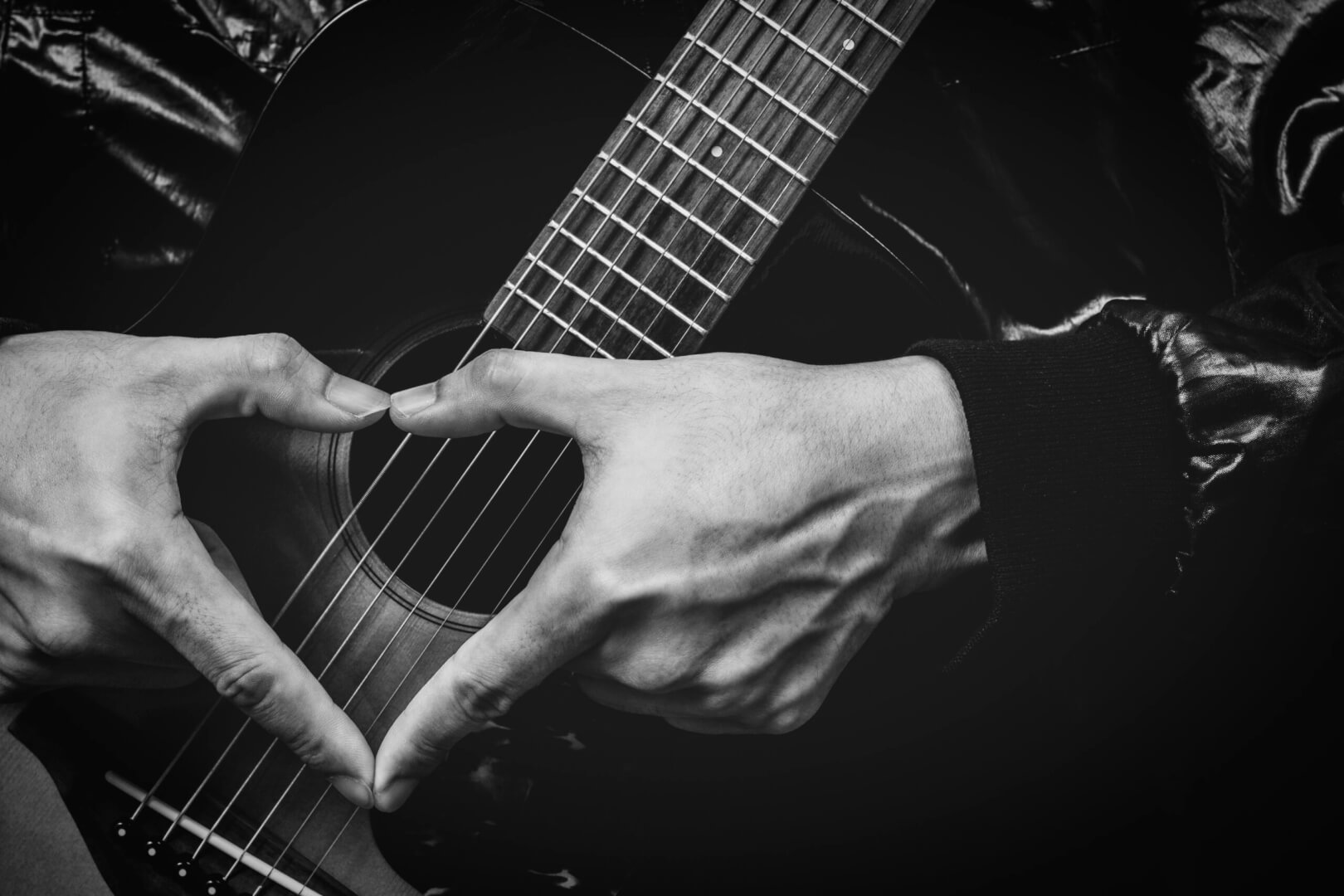 Una imagen en blanco y negro con una guitarra y unas manos recreando la imagen de un corazón para hablar de la música de los años 60 en España.