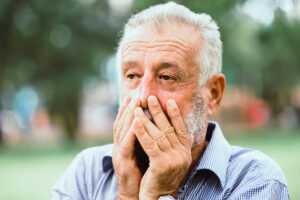 Primer plano de un anciano con las manos en la cara estresado.