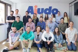 El equipo de Aiudo formado por 19 personas posando en una sala con las letras de Aiudo detrás de ellos.