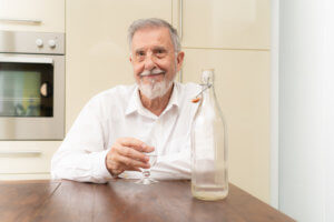 Persona mayor bebiendo un vaso de agua desde una botella de vidrio