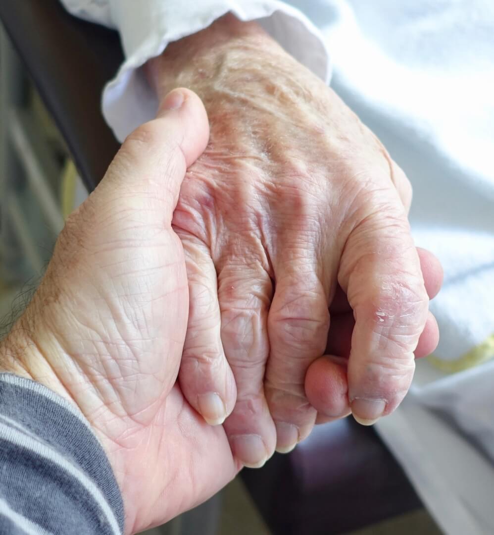 Un primer plano de las manos de cuidador no profesional agarrando las de su madre anciana. 