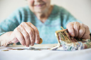 Manos de una mujer mayor, con una sostiene un monedero y con la otra una moneda.