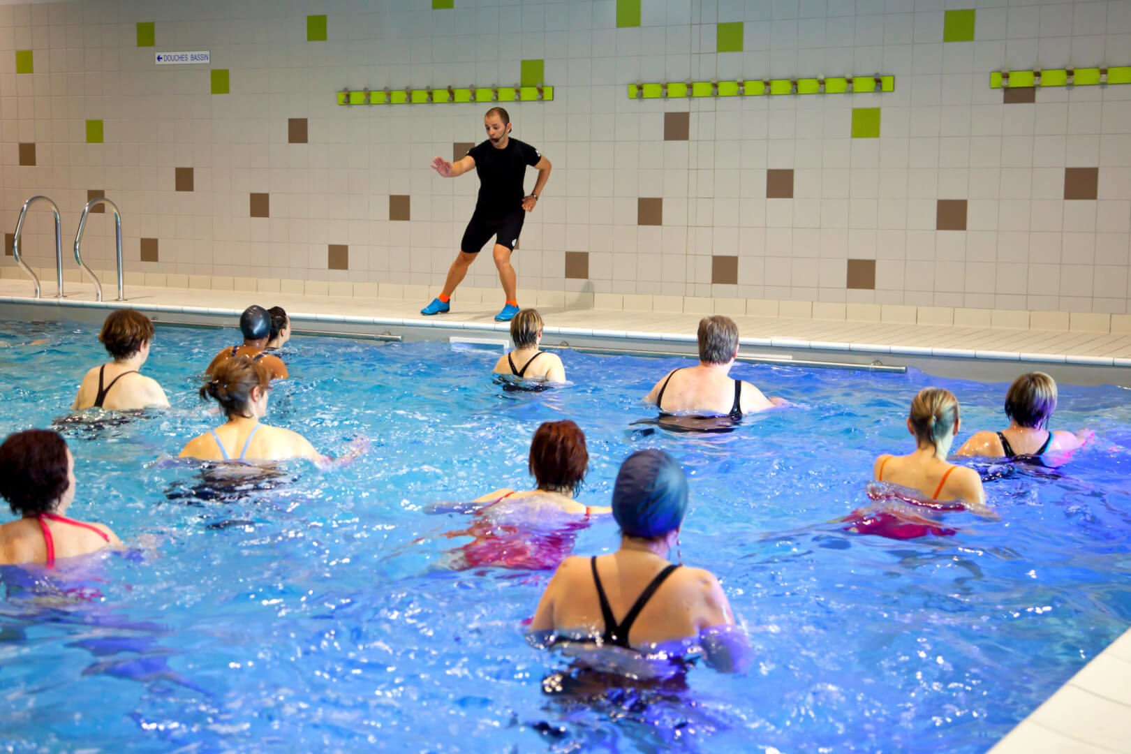 En la imagen aparece un monitor de aquagym practicando un ejercicio ante la atenta mirada de sus alumnas, mujeres mayores que quieren practicar ejercicios de aquagym. 