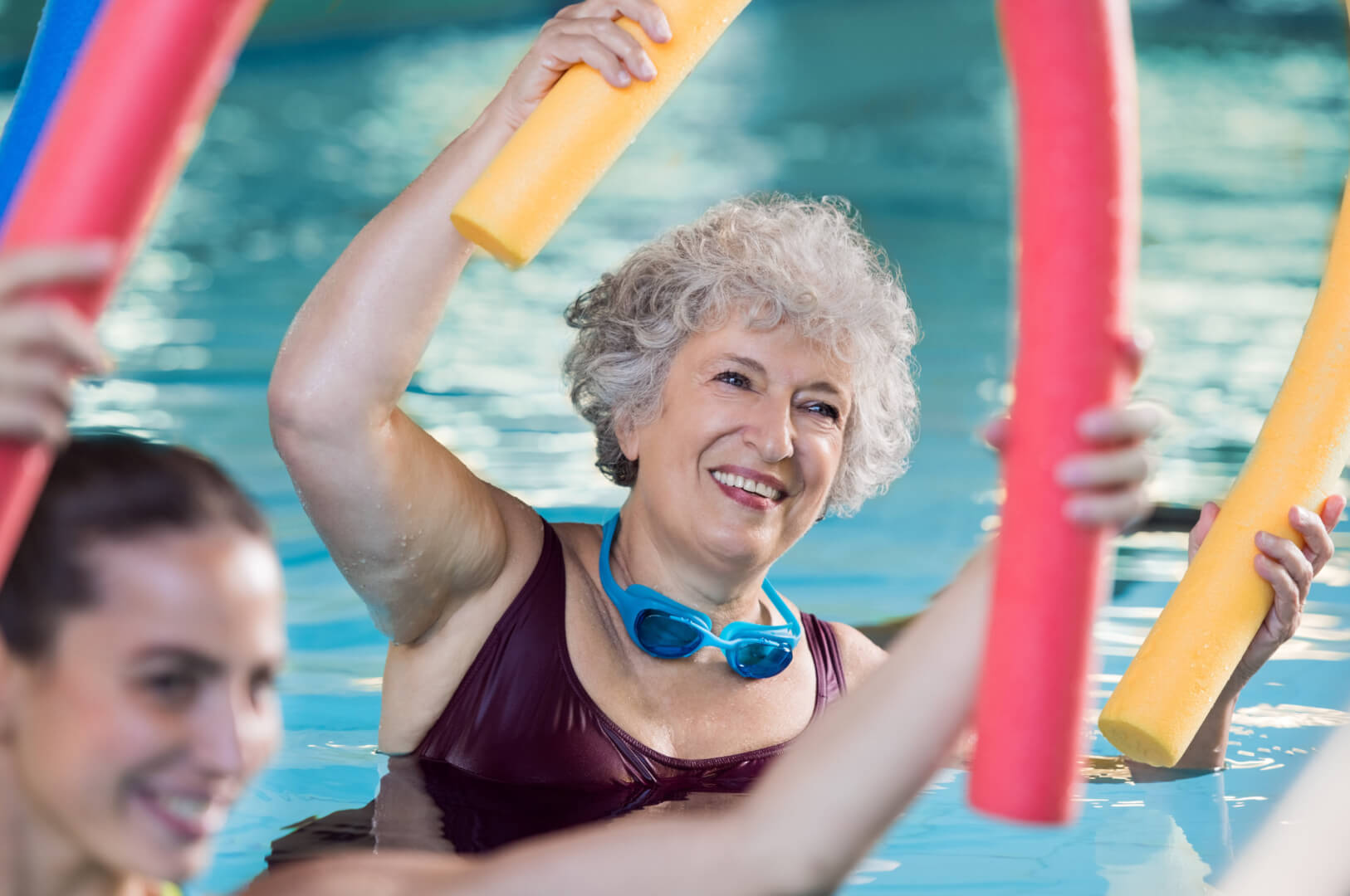 En la imagen aparece una mujer mayor sonriendo mientras practica aquagym en una piscina climatizada. 