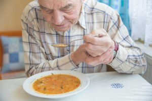 Un hombre mayor a punto de tomar una sopa de verduras con una cuchara en la mano.