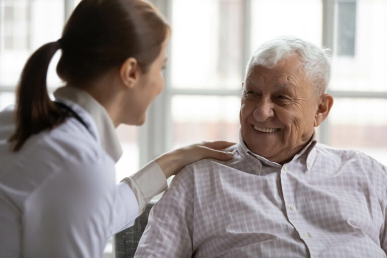 Un hombre mayor sonriendo a una enfermera que lo toma del hombro.