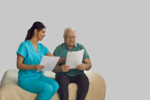 Un hombre mayor sentado junto a una enfermera sosteniendo ambos un papel. Ella está señalando el del hombre.