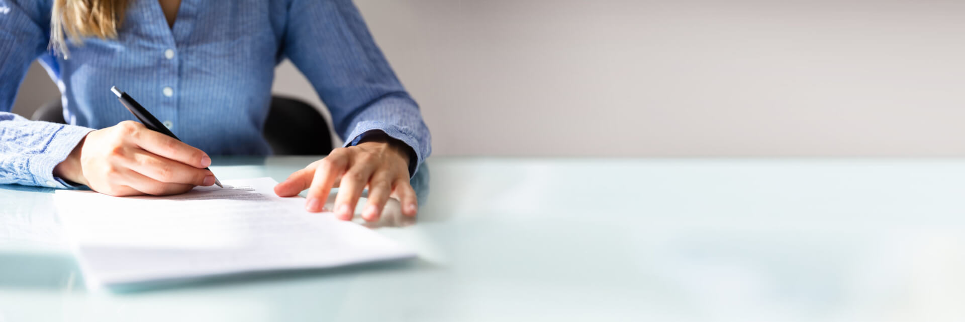 En la imagen, una mujer adulta que ostenta un alto cargo gubernamental firma un documento sobre políticas de empleo. Es un plano corto de las manos de la mujer en una mesa y un documentoi.