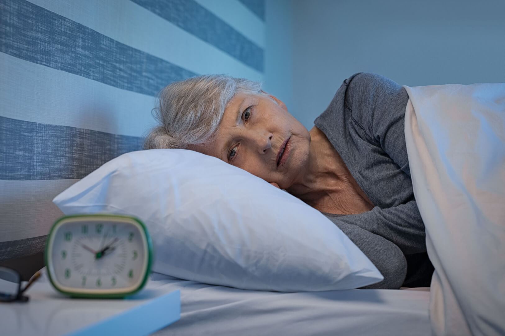 Una mujer de edad avanzada se muestra triste sobre su cama en la noche ante la incapacidad de conciliar el sueño debido a la nictofobia que padece. 