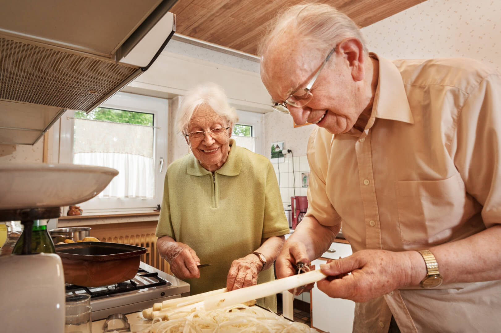 Un hombre mayor prepara un plato de cocina bajo la atenta mirada de su mujer, que lo mira riéndose