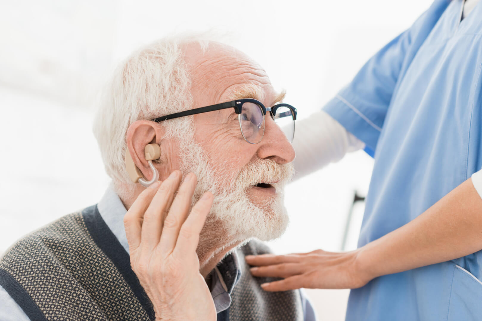 Un anciano se sostiene el audífono mientras una experta sanitaria le toca los hombros como muestra de afecto ante el momento de colocación del dispositivo auditivo.