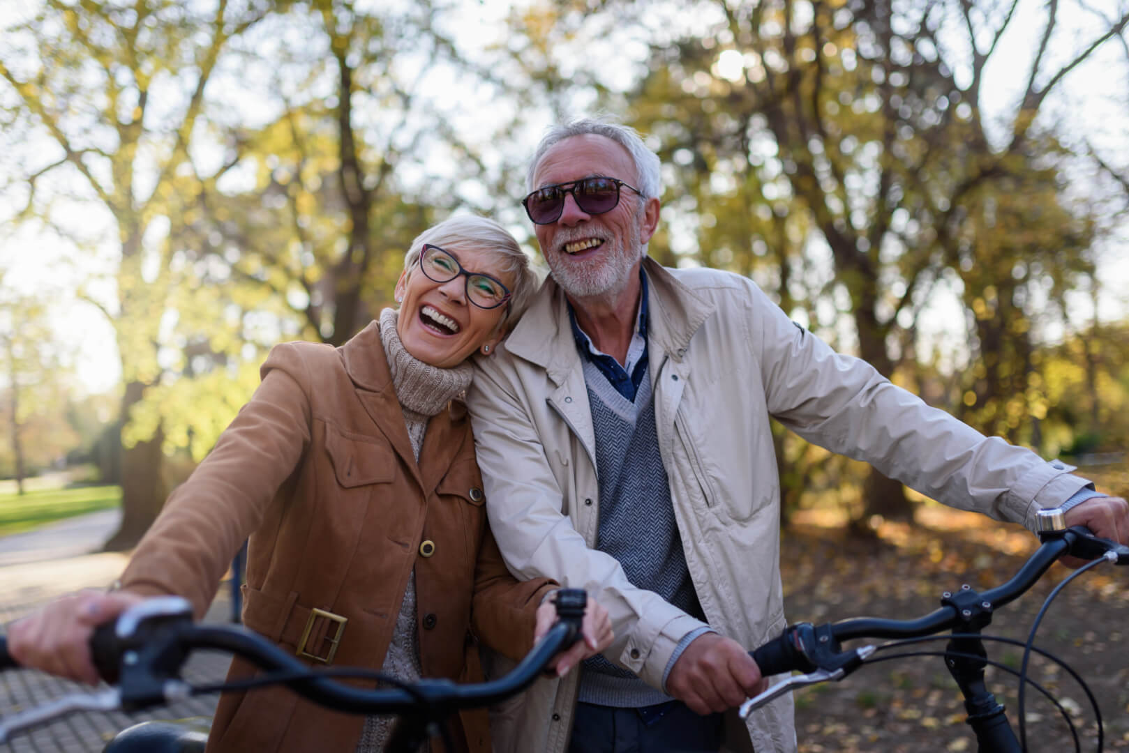 En la imagen aparecen un matrimonio de dos personas mayores riendo y montando en bicicleta en un parque en un claro gesto de vitalidad de las nuevas generaciones de la tercera edad.
