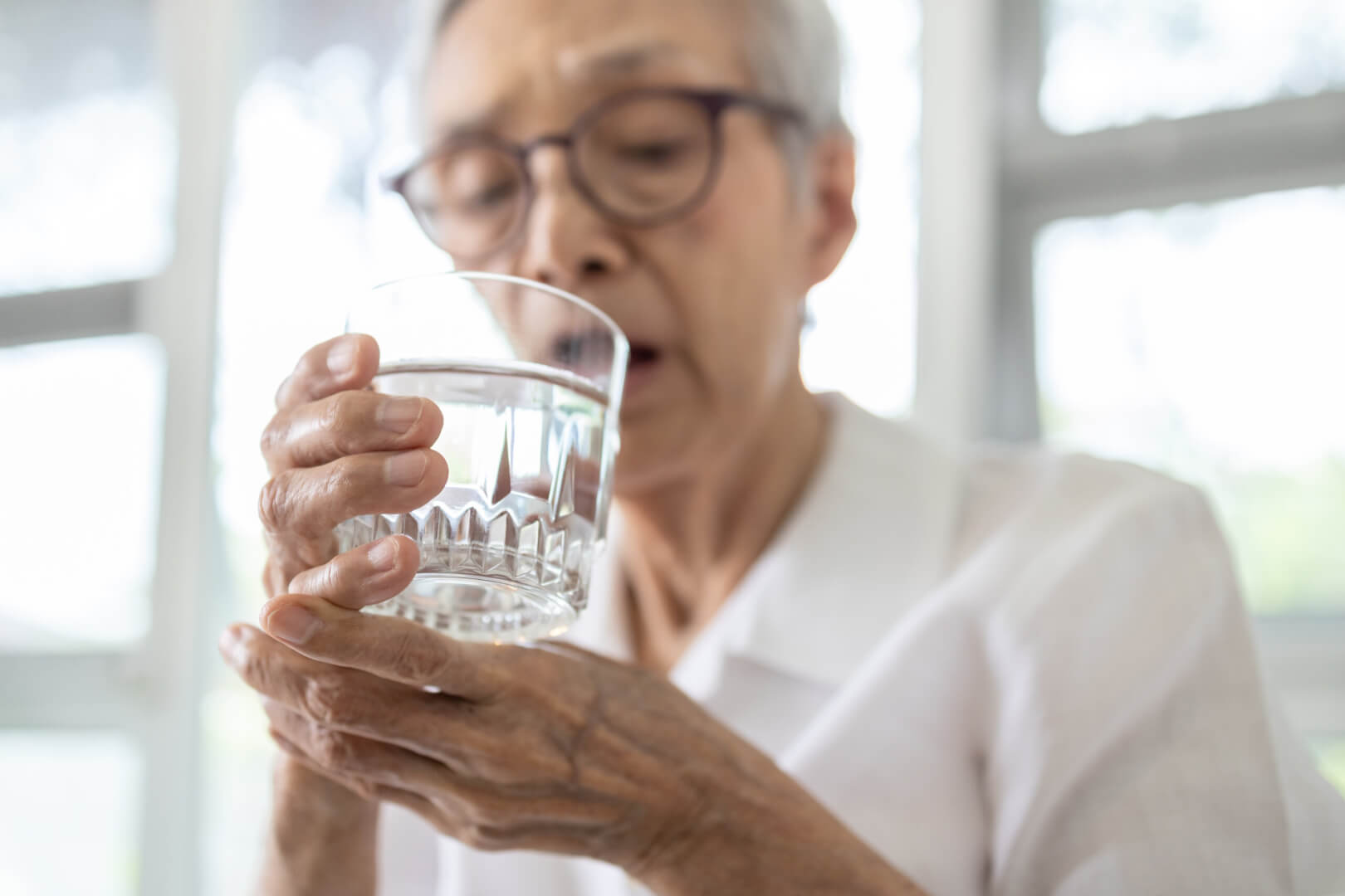 Una mujer mayor tiene dificultades para sujetar un vaso con agua ante un problema de sarcopenia. 