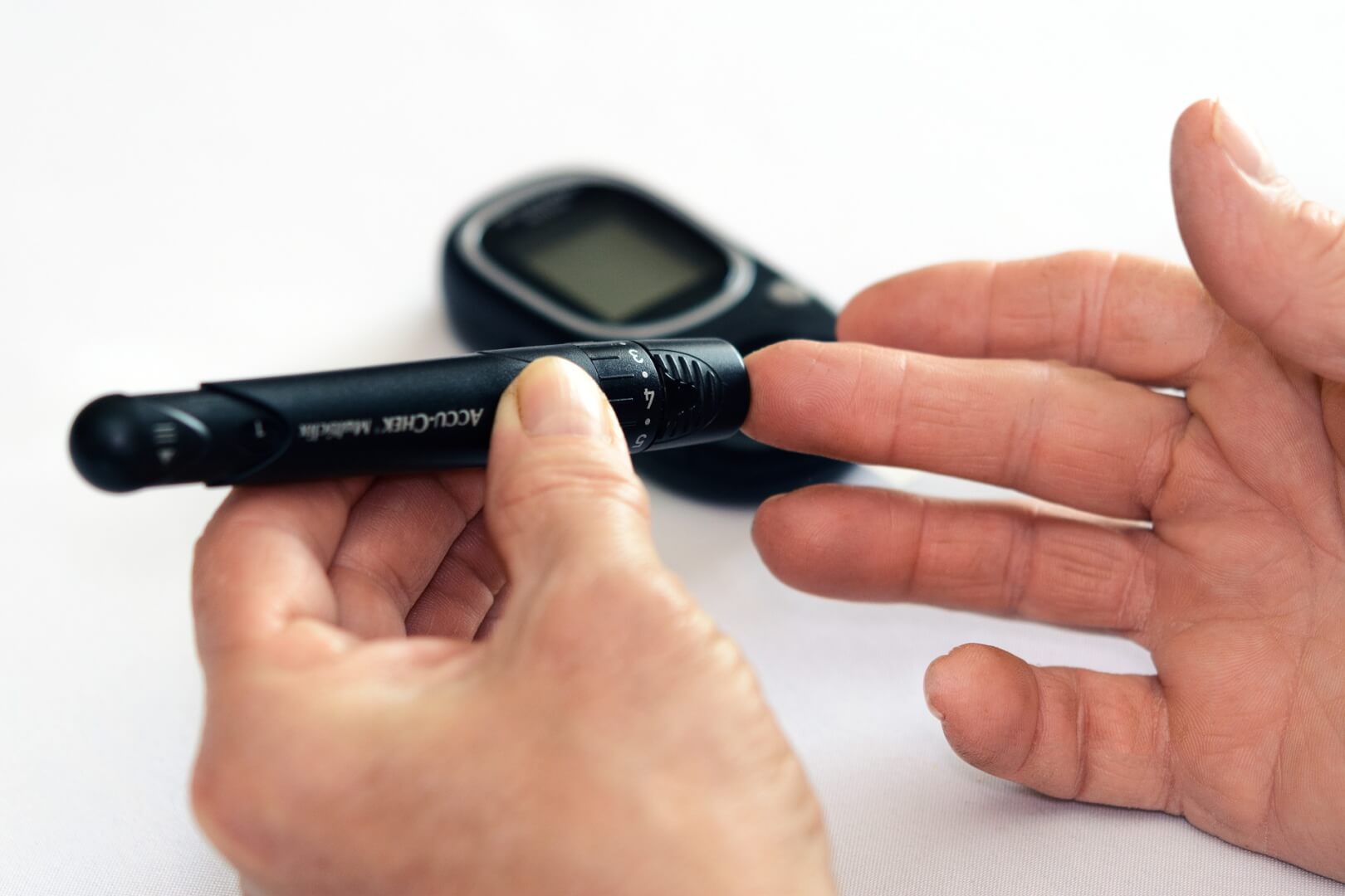 Unas manos de una persona mayor. Se muestra un aparato, llamado glucómetro, que mide el nivel de azúcar en sangre.