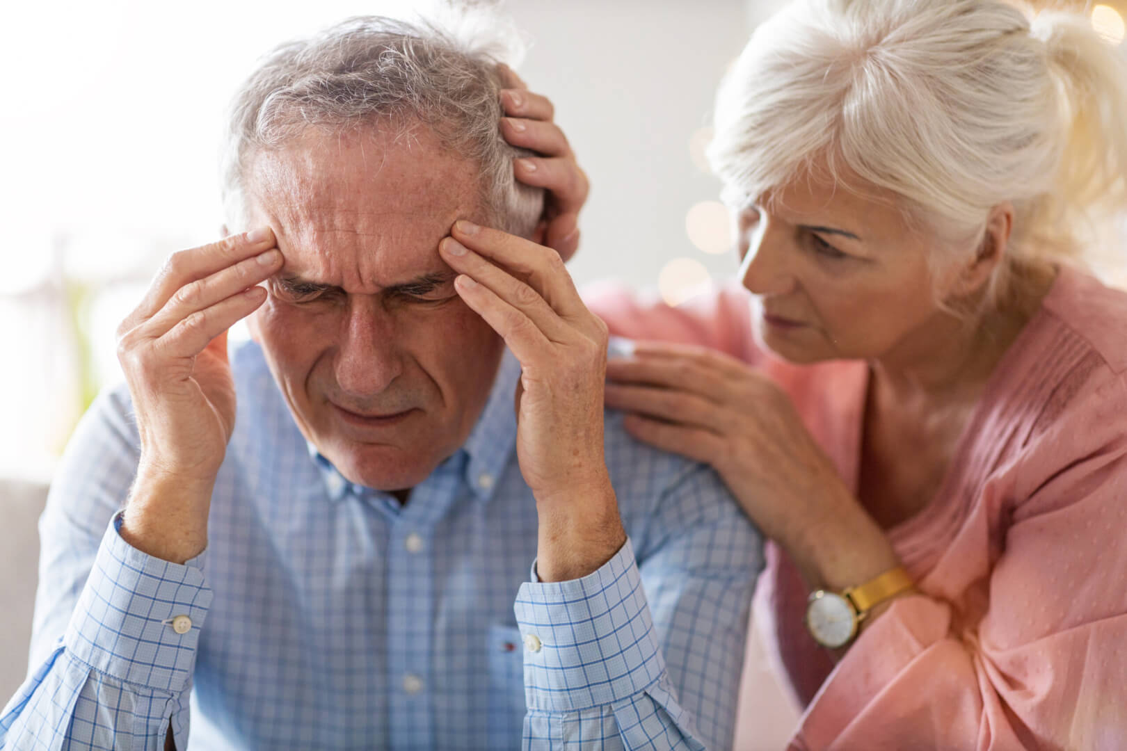 Una mujer mayor consuela a su marido que se queja de un dolor de cabeza constante y que le hace tener un mal comportamiento. 