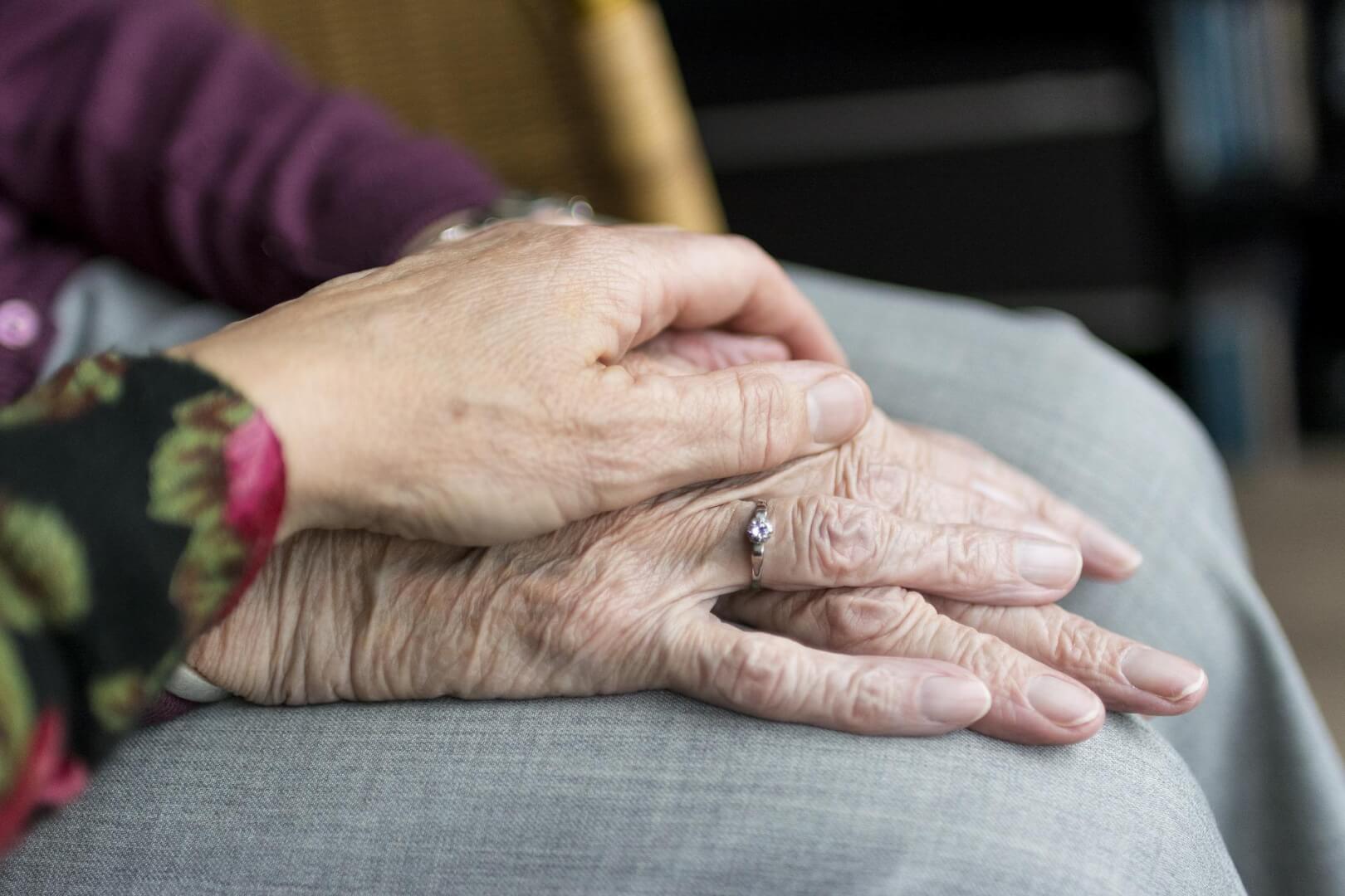 Unas manos de una cuidadora cogen las manos de una anciana. Es un primer plano de una manos. 