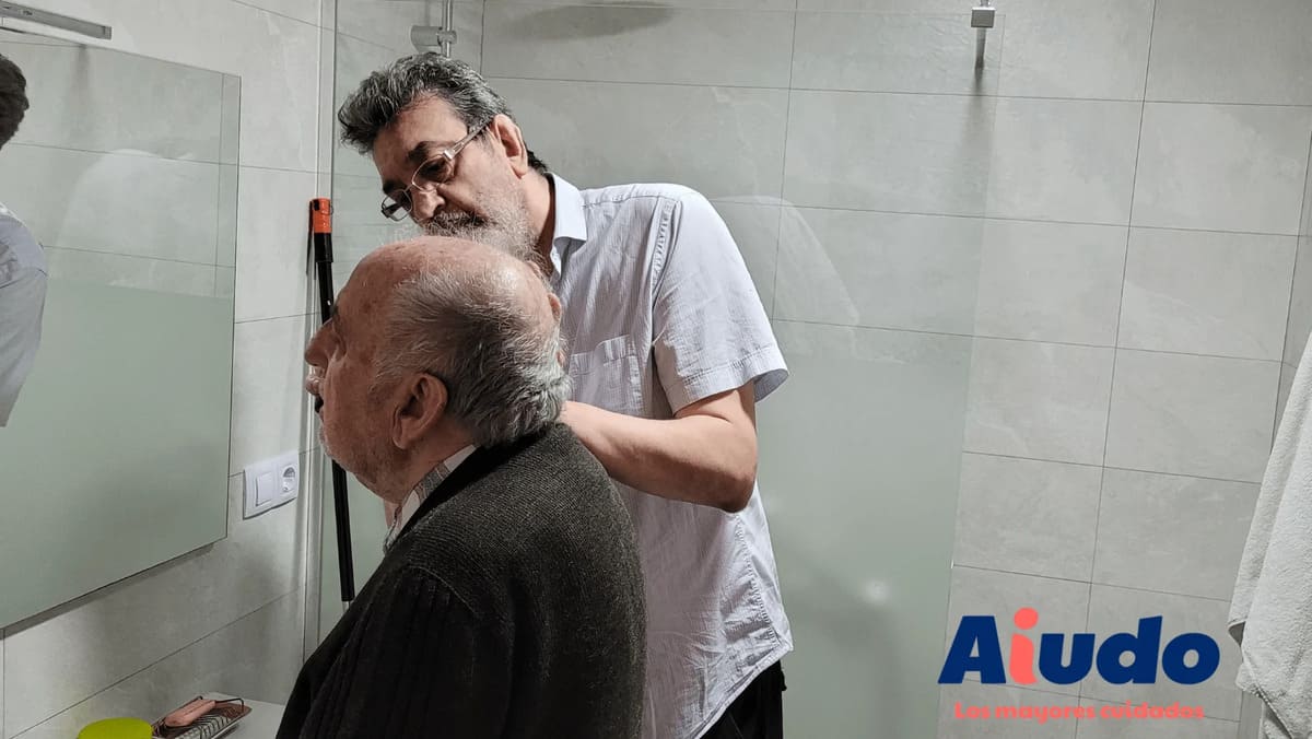 Un cuidador hombre ayudando a afeitar a persona mayor.