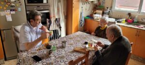 2 ancianos desayunan en la mesa de la cocina junto a un hombre.
