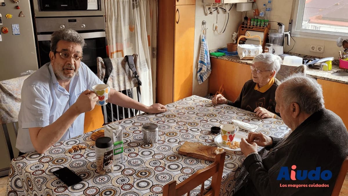 Hombre cuidador junto a dos ancianos en la cocina tomando café