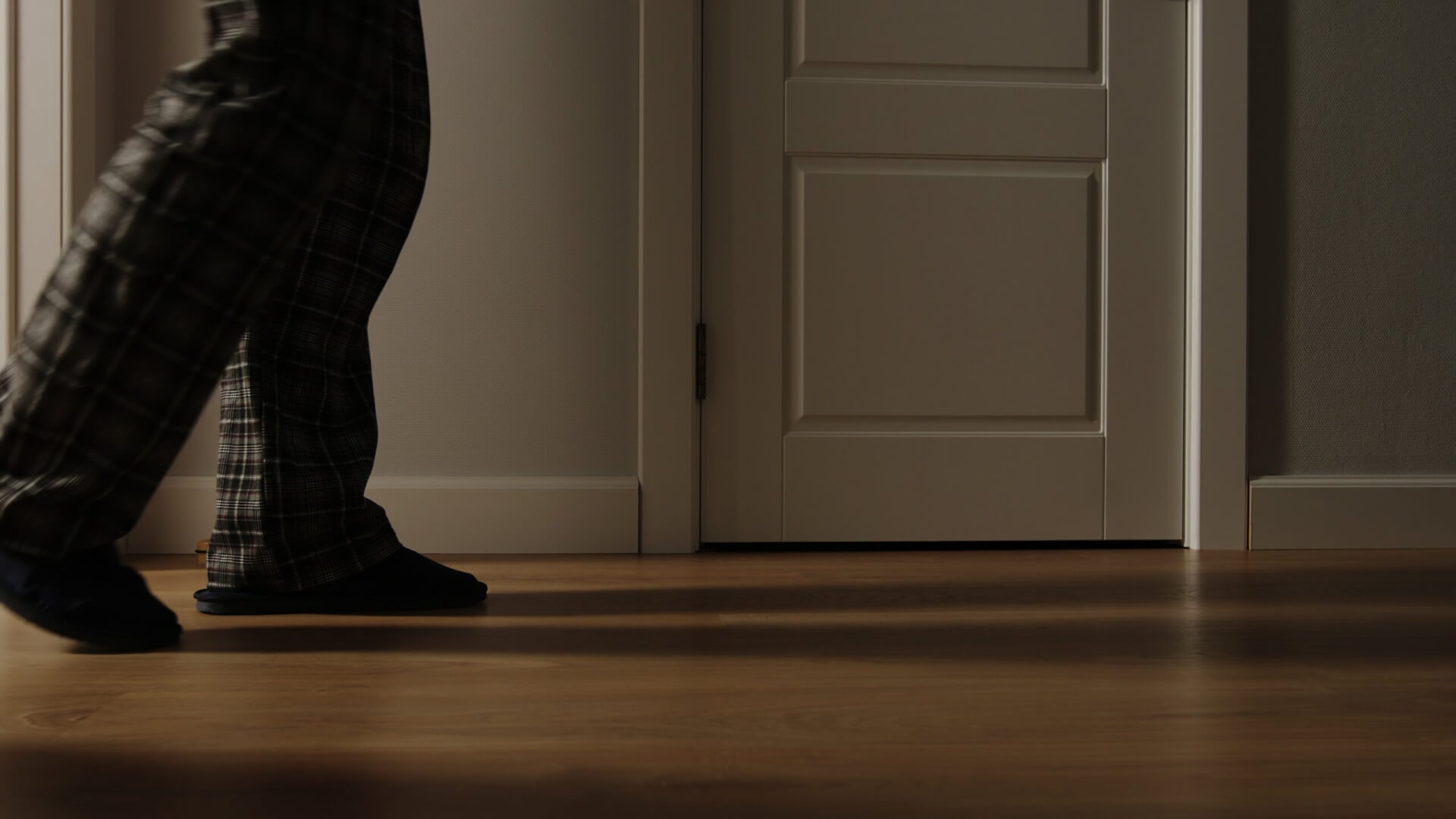 Un anciano camina por su casa algo desorientado. En un plano corto de sus piernas y pies solamente, portando unas zapatillas de estar en casa.